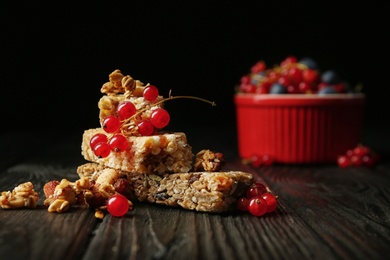 Photo of Different grain cereal bars and red currant on wooden table against black background