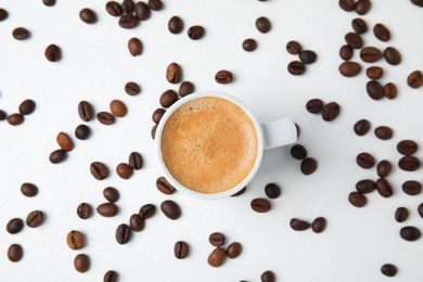 Photo of Cup of tasty espresso and scattered coffee beans on white table, flat lay