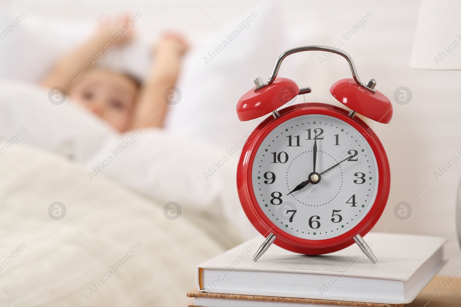 Photo of Cute little girl awaking in cosy bed, focus on alarm clock