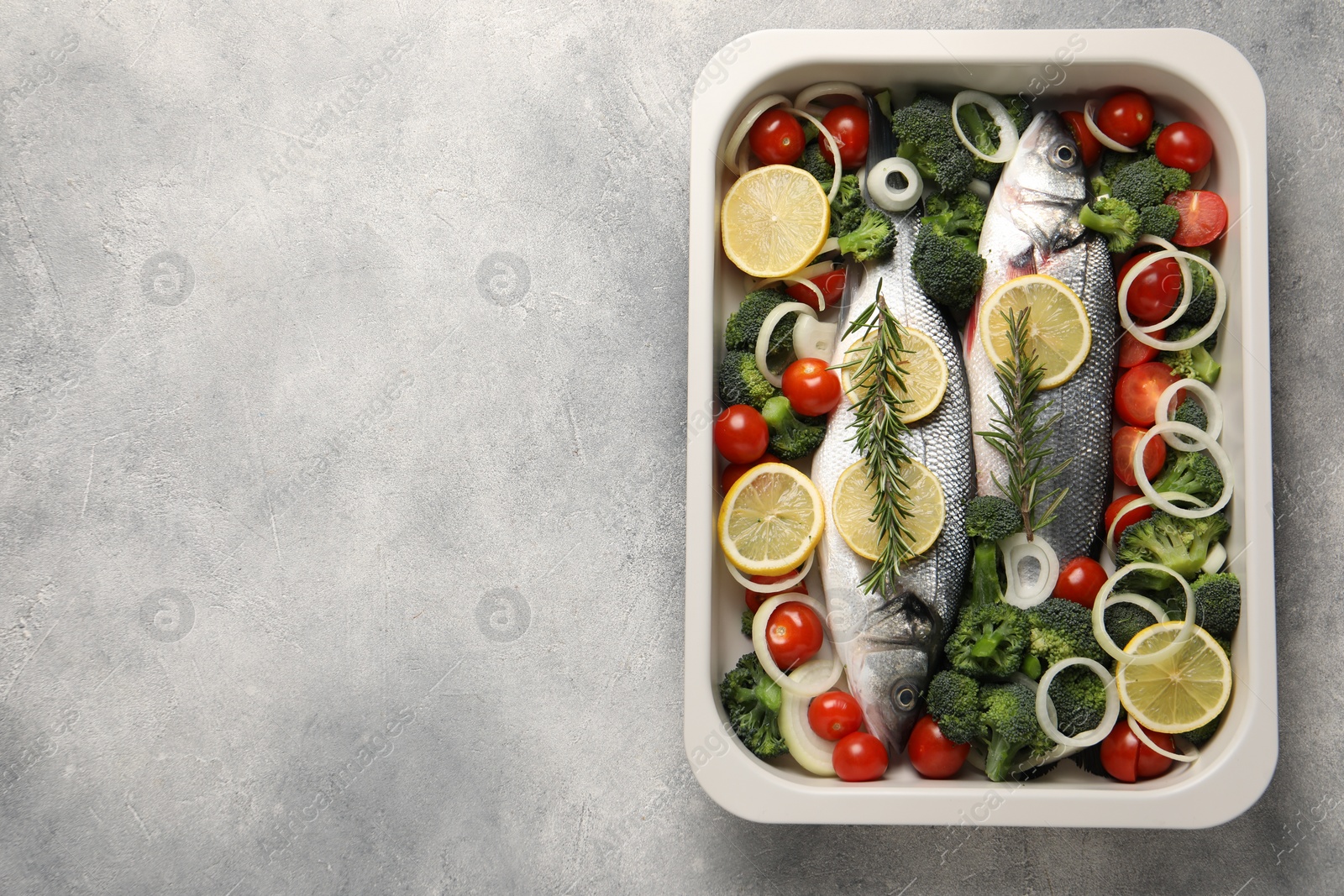 Photo of Raw fish with vegetables and lemon in baking dish on grey textured table, top view. Space for text