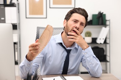 Photo of Bearded businessman waving hand fan to cool himself at table in office