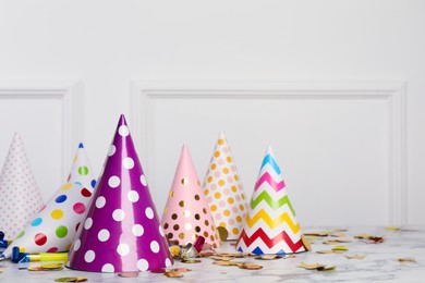 Colorful party hats and festive items on marble table near white wall indoors. Space for text