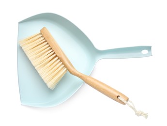 Photo of Light blue dustpan and wooden brush on white background, top view