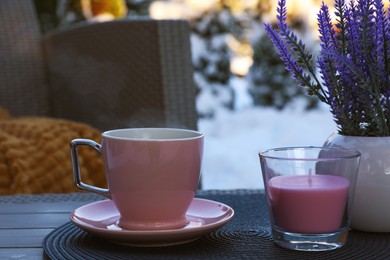 Candle, potted flowers and cup of hot drink on coffee table outdoors. Cosy winter