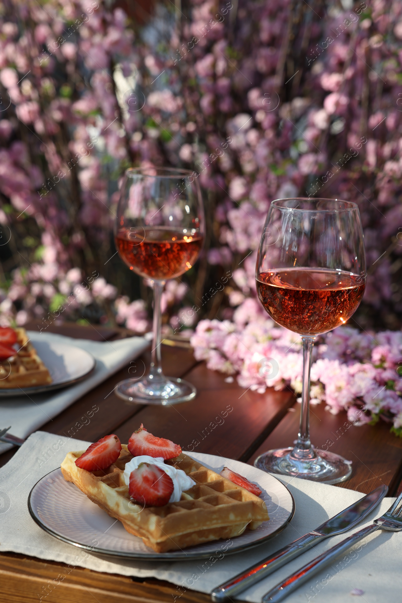 Photo of Delicious Belgian waffles with fresh strawberries and wine served on table in garden