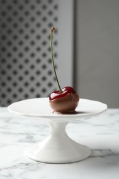 Photo of Sweet chocolate dipped cherry on white marble table