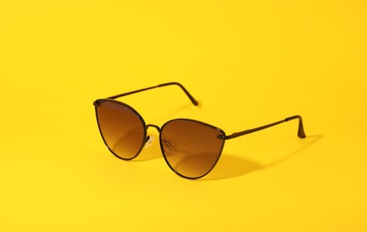 Photo of Stylish pair of sunglasses on yellow background