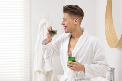 Photo of Young man using mouthwash in bathroom. Oral hygiene