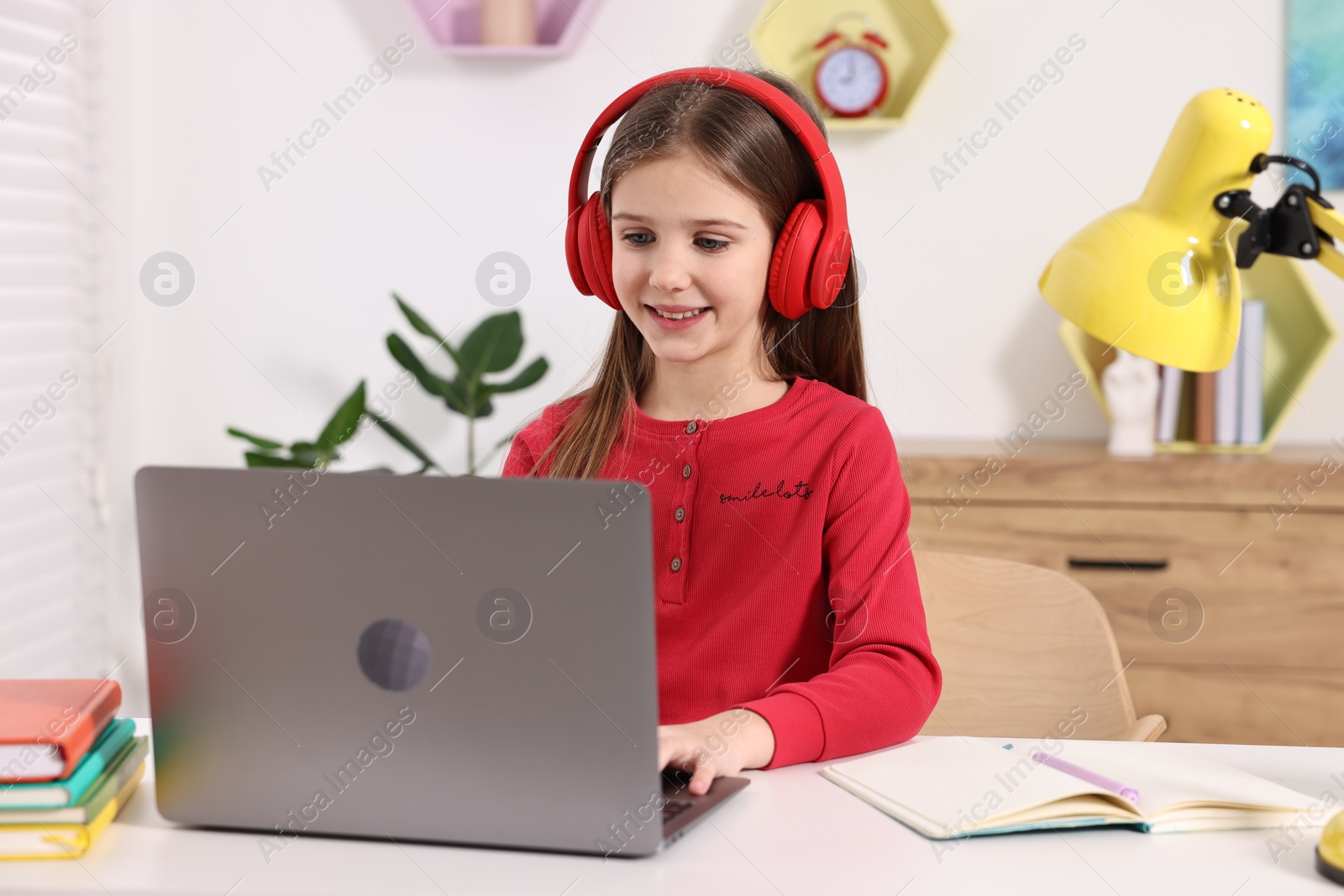 Photo of E-learning. Cute girl using laptop and headphones during online lesson at table indoors