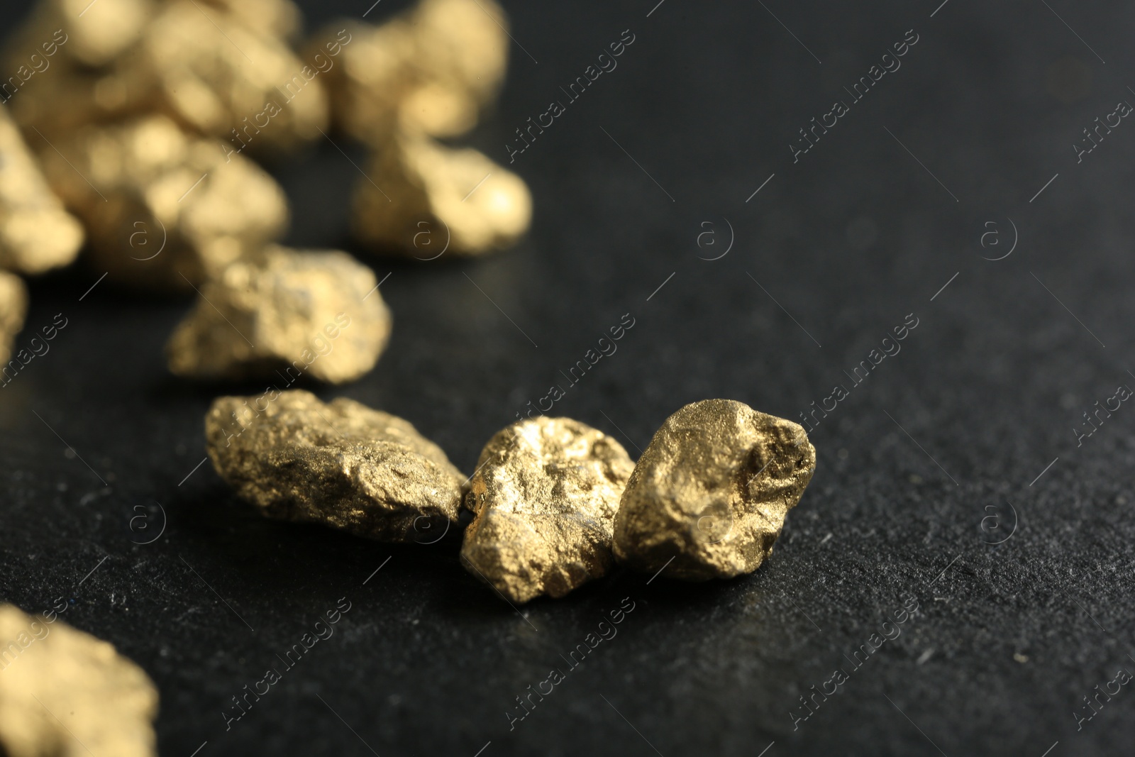 Photo of Shiny gold nuggets on grey textured surface, closeup. Space for text