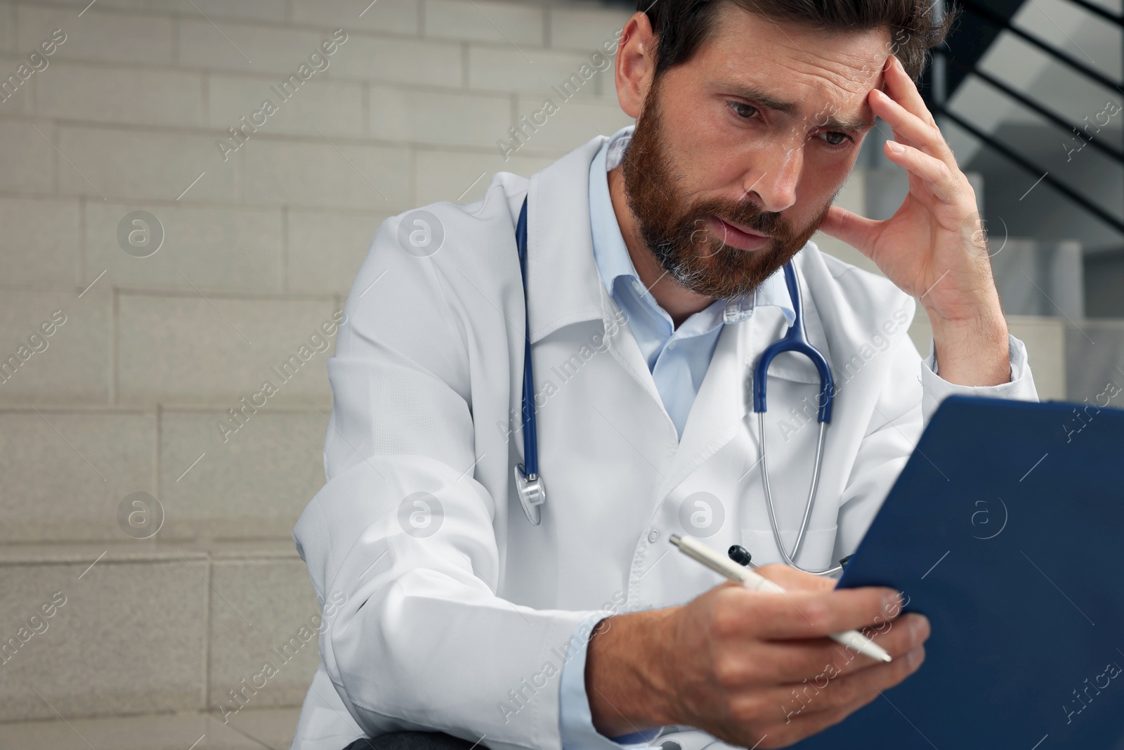 Photo of Upset doctor with clipboard sitting on stairs in hospital