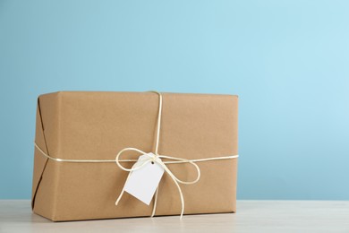 Photo of Parcel wrapped in kraft paper with tag on white wooden table against light blue background