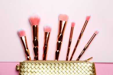 Photo of Bag with different makeup brushes on color background, flat lay