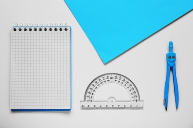 Photo of Protractor ruler, paper sheet, notebook and compass on white background, flat lay