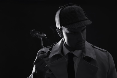Photo of Old fashioned detective smoking pipe on dark background, black and white effect