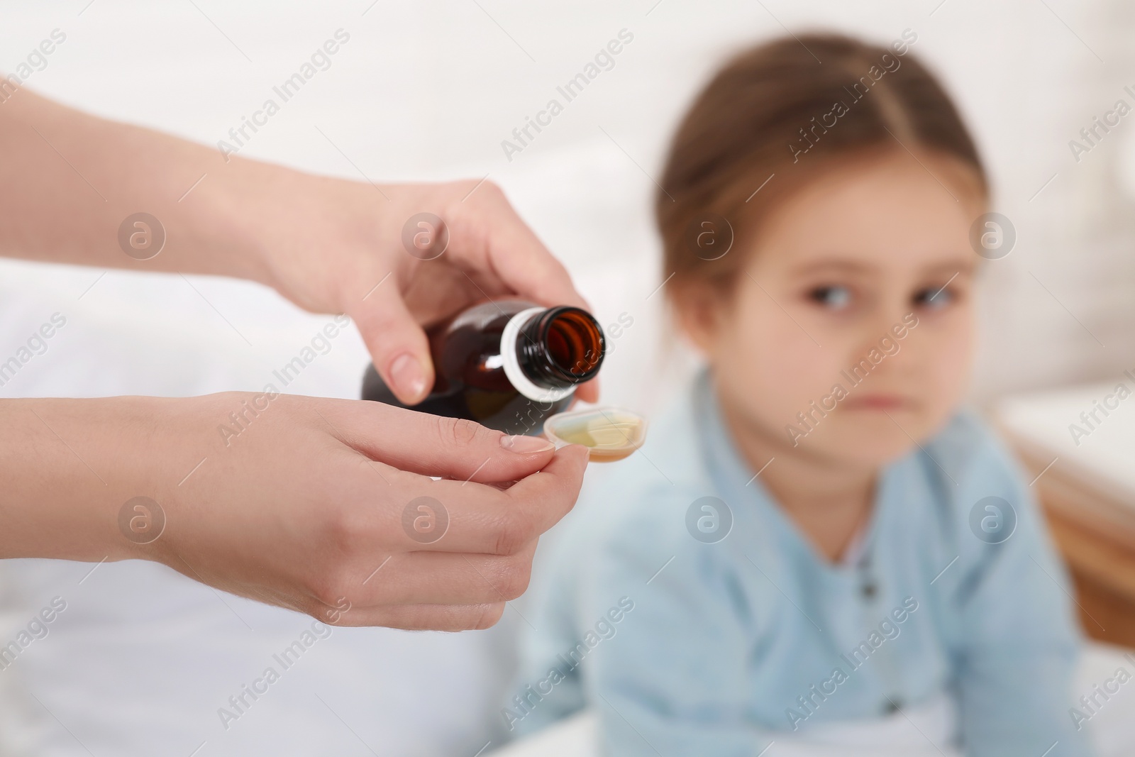 Photo of Mother pouring cough syrup into measuring spoon for her daughter indoors, focus on hands