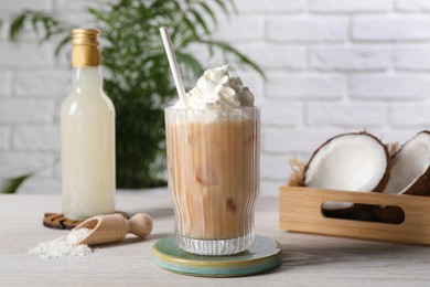 Photo of Bottle of delicious syrup, glass of iced coffee, halves of coconut and flakes on white wooden table