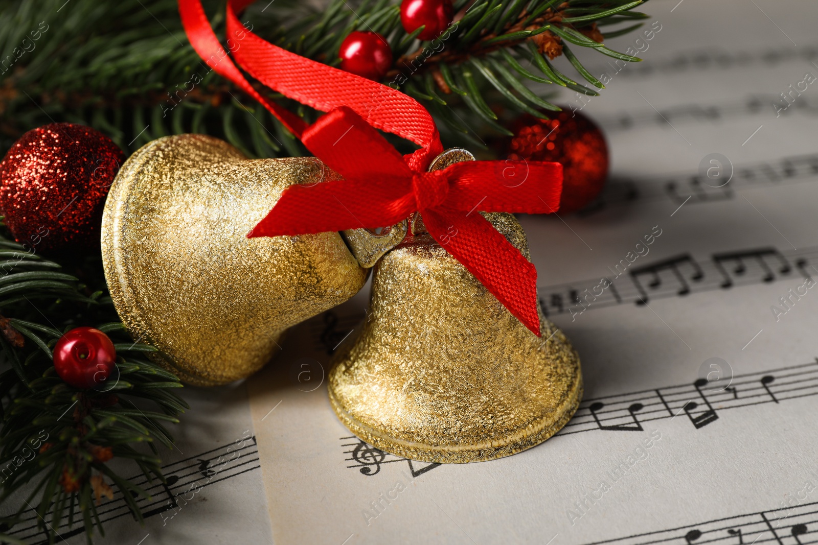 Photo of Golden shiny bells and fir branches with Christmas decor on music sheets, closeup