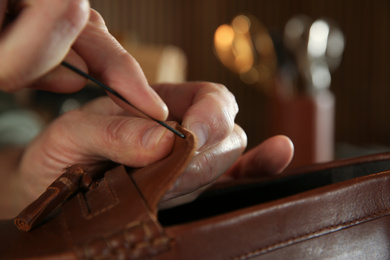 Photo of Man working with leather shoes in workshop, closeup