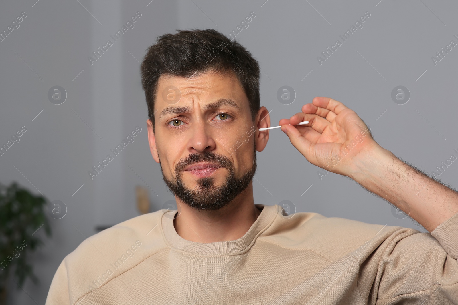 Photo of Emotional man cleaning ears and suffering from pain in room