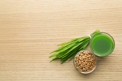 Photo of Shot glass of wheat grass juice, bowl with grains and sprouts on wooden table, flat lay. Space for text