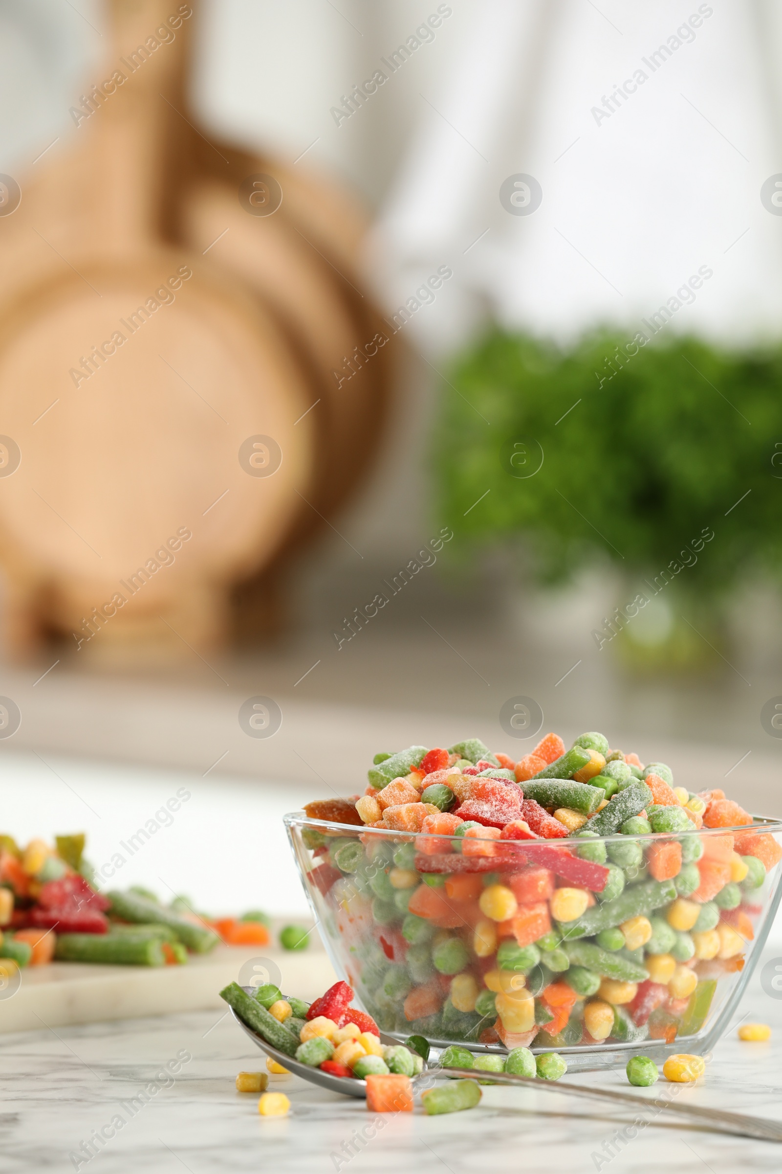 Photo of Mix of different frozen vegetables in glass bowl on white marble countertop in kitchen. Space for text