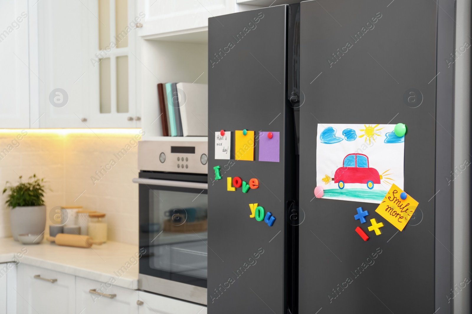 Photo of Modern refrigerator with child's drawing, notes and magnets in kitchen