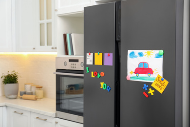 Modern refrigerator with child's drawing, notes and magnets in kitchen