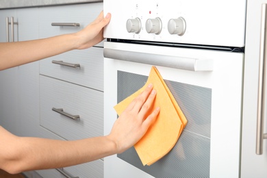 Photo of Woman cleaning electric oven with rag in kitchen, closeup