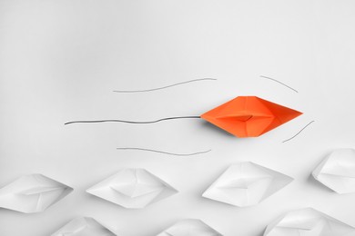 Photo of Orange paper boat floating past others on white background, flat lay. Uniqueness concept