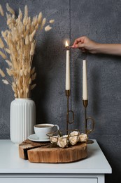 Photo of Woman lighting candle on table near grey wall indoors, closeup. Interior design