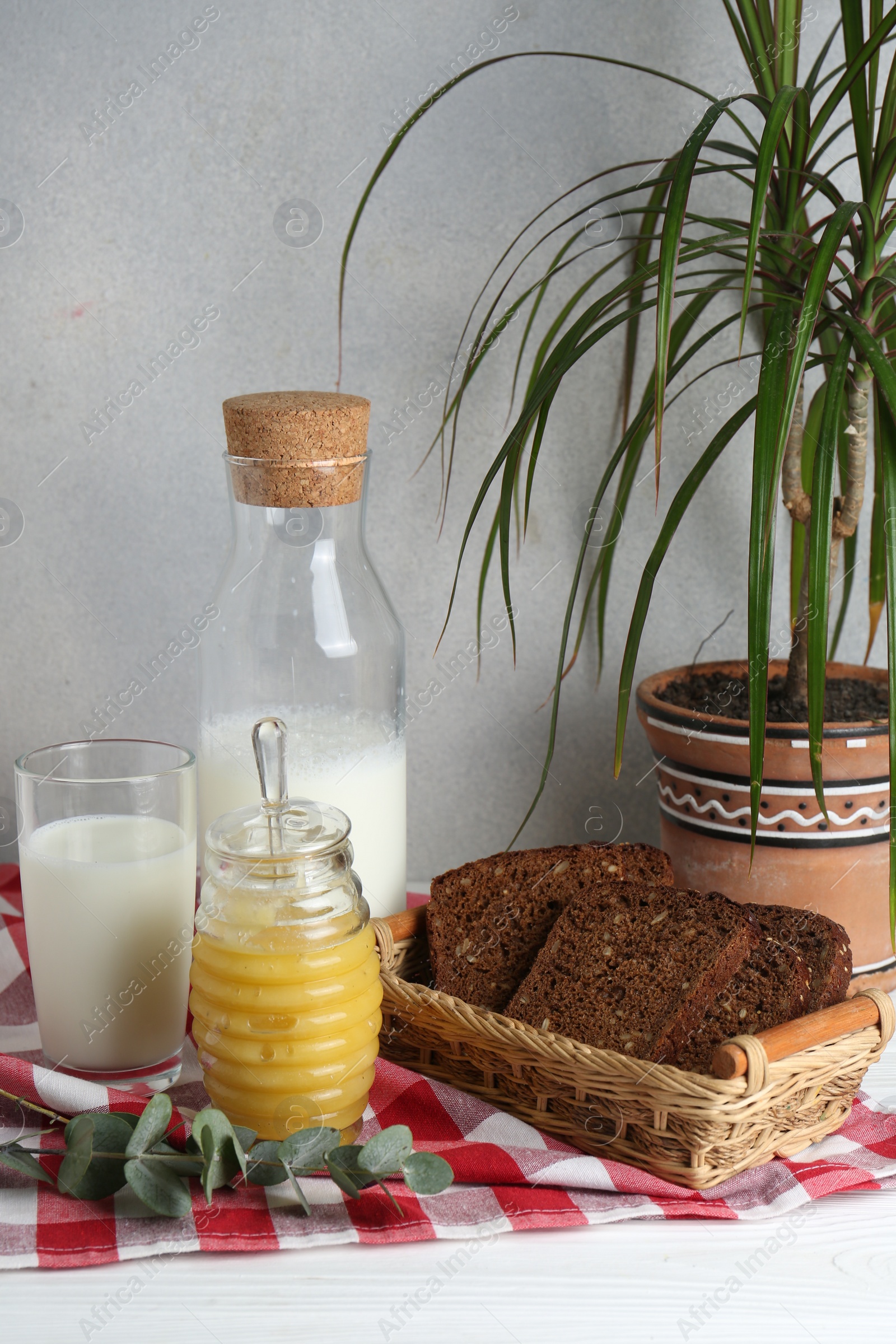 Photo of Jar with tasty honey, milk and bread on white wooden table