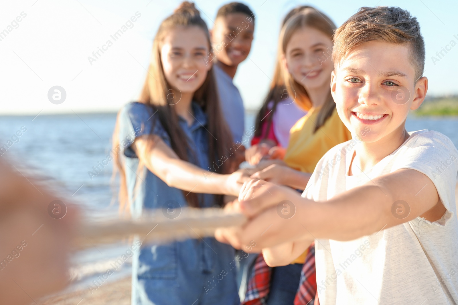 Photo of Group of children pulling rope during tug of war game on beach. Summer camp