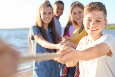 Photo of Group of children pulling rope during tug of war game on beach. Summer camp