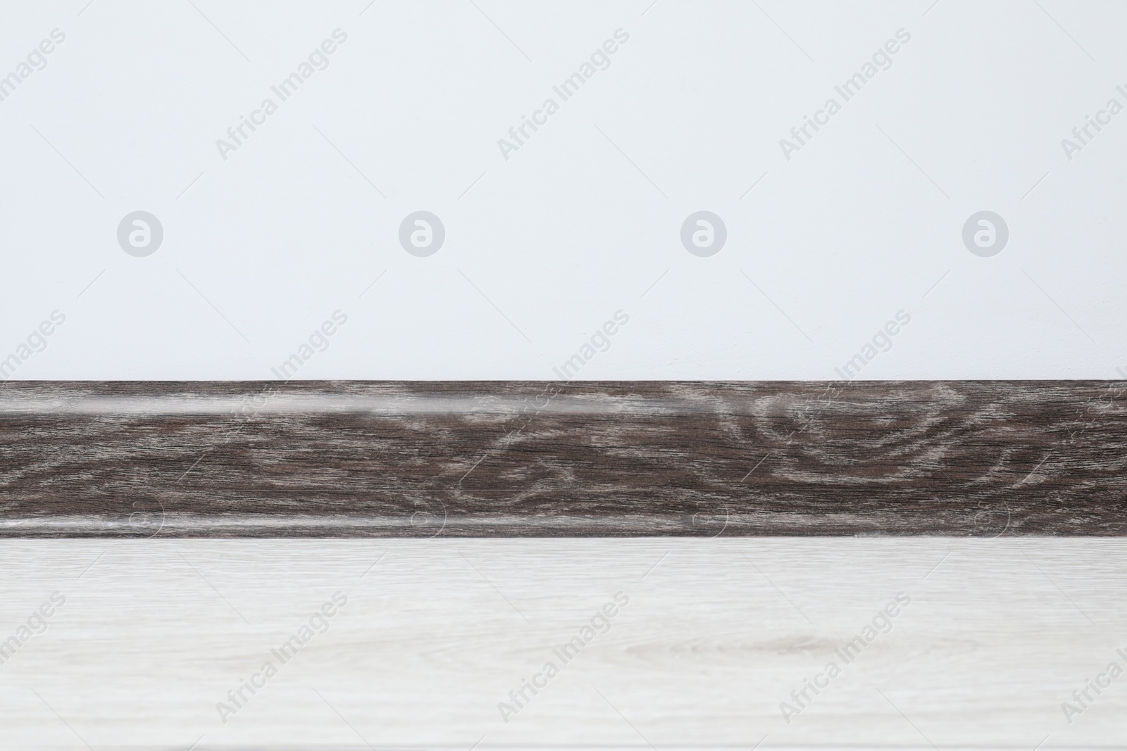 Photo of Black wooden plinth on laminated floor near white wall indoors