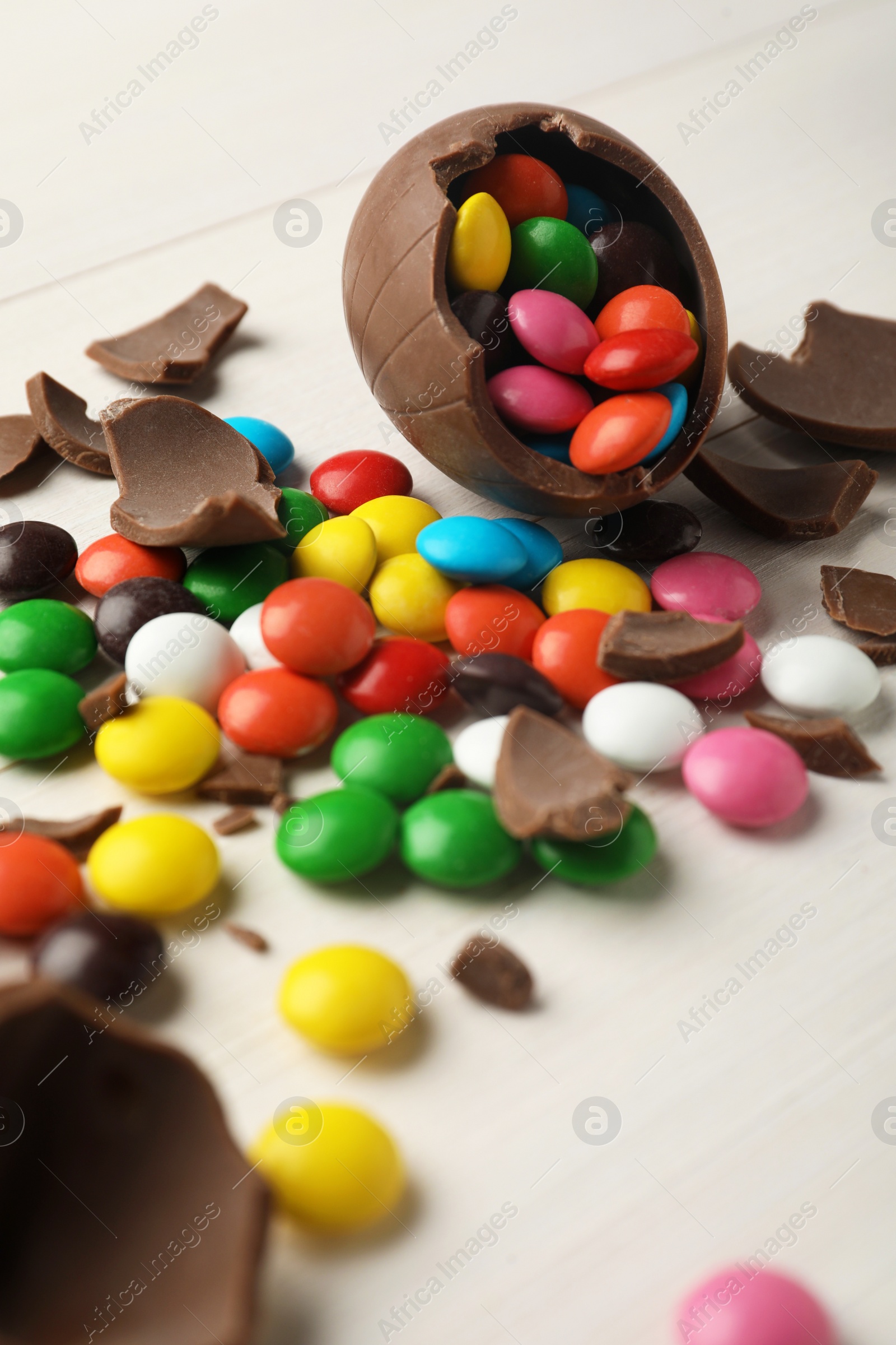 Photo of Broken chocolate egg and colorful candies on white table