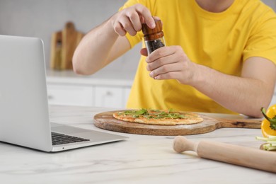 Man adding pepper on pizza while watching cooking online course in kitchen, closeup. Time for hobby