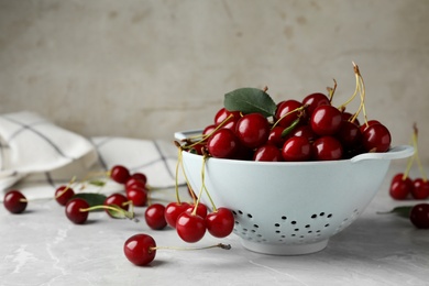 Colander of tasty ripe cherries on grey marble table