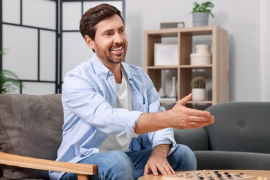 Photo of Happy man offering handshake after playing checkers at home