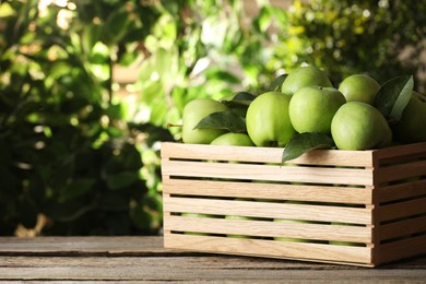 Photo of Crate full of ripe green apples and leaves on wooden table outdoors. Space for text