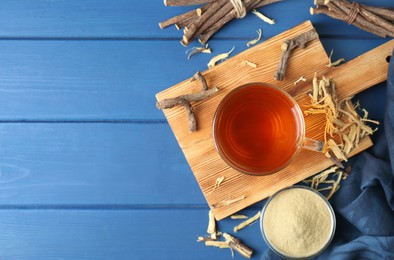 Photo of Aromatic licorice tea in cup, dried sticks of licorice root and powder on blue wooden table, flat lay. Space for text