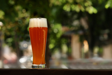 Photo of Glass of tasty beer on railing outdoors, space for text