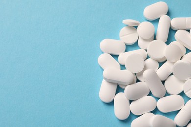 Photo of Pile of white pills on light blue background, flat lay. Space for text