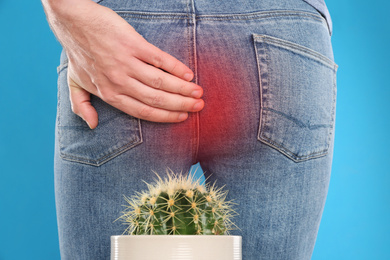 Image of Man sitting down on cactus against light blue background, closeup. Hemorrhoid concept