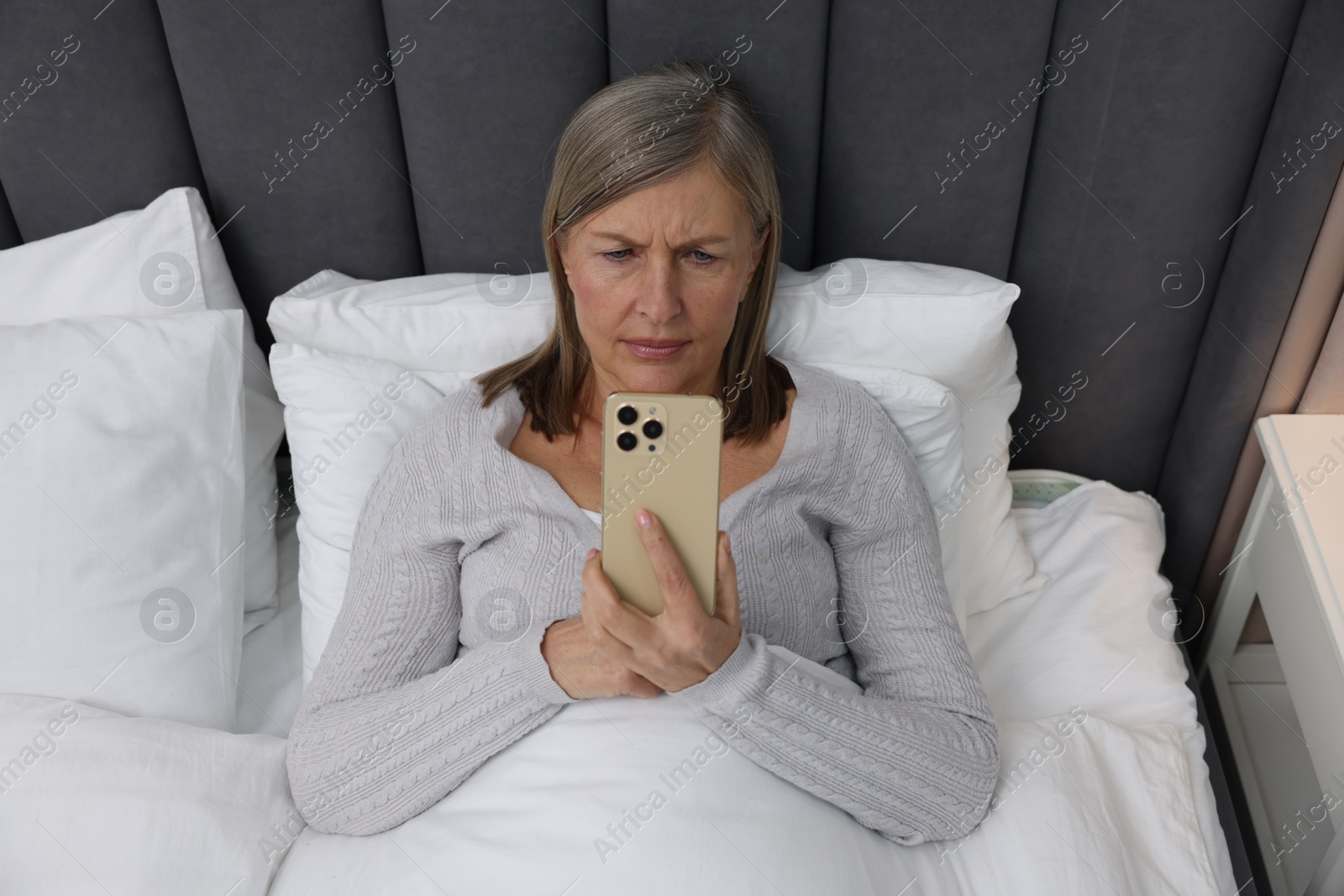 Photo of Menopause. Sleepless woman using smartphone in bed indoors