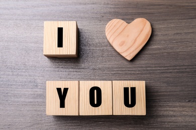 Photo of Phrase I love You made of decorative heart and cubes on wooden background, flat lay