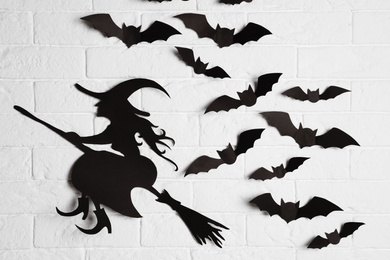 Photo of Paper bats and witch cutout on brick wall. Halloween decor