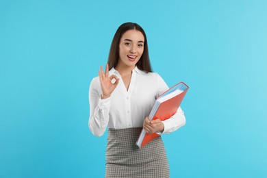 Happy woman with folder showing OK gesture on light blue background