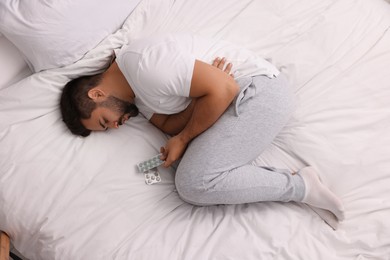 Photo of Depressed man with antidepressants on bed, top view