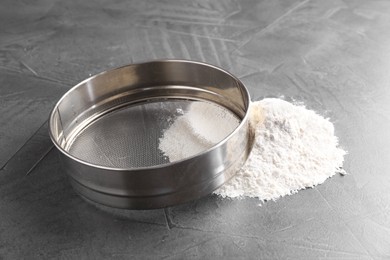 Photo of Metal sieve and flour on grey table